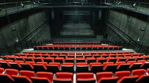 Interior del auditorio con butacas rojas dispuestas en gradas y escenario oscuro