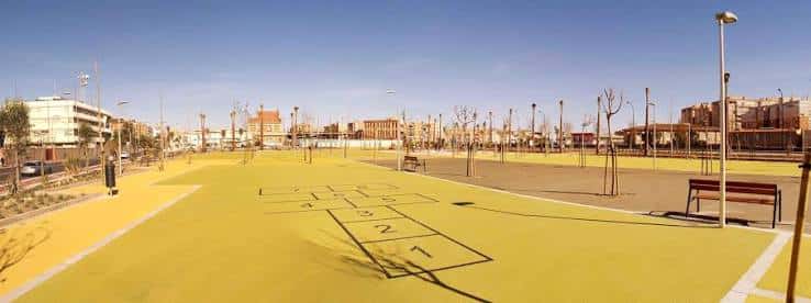 Amplia zona de juegos infantiles con suelo amarillo y juegos tradicionales