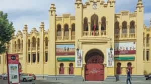 Entrada principal de la Plaza de Toros de Albacete con carteles publicitarios y personas caminando