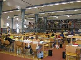 Interior de la biblioteca con mesas de lectura y estanterías llenas de libros