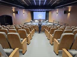 Interior del auditorio con pantalla de proyección y disposición de asientos