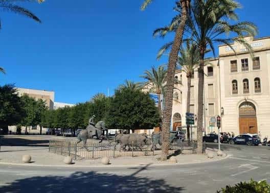 Vista de la Plaza de España con la fuente de los elefantes y palmeras bajo un cielo despejado
