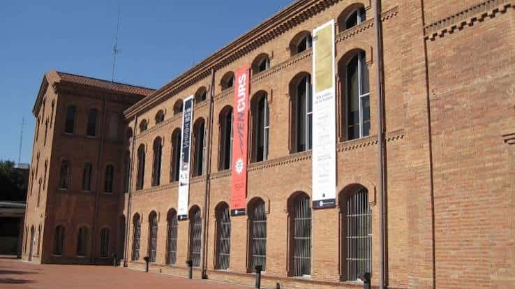 Fachada lateral del edificio de Tecla Sala con banderas de exposiciones y arquitectura industrial restaurada