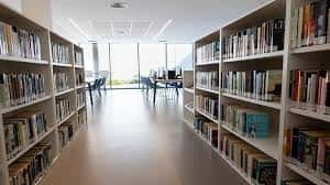 Pasillo central de la biblioteca con estanterías a ambos lados y ventana al fondo