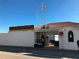 Entrada principal del Club Nàutic Bétulo con fachada blanca y banderas