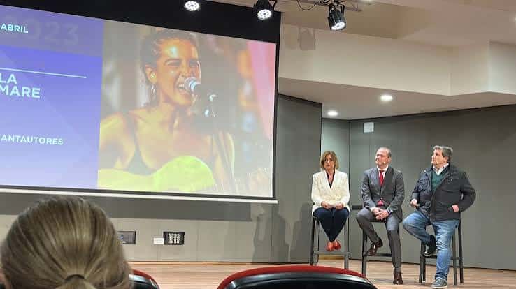 Panel de discusión en el escenario del centro cultural con proyección de artista en pantalla