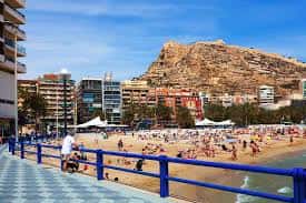 Playa del Postiguet con bañistas, sombrillas blancas y el monte Benacantil en el horizonte