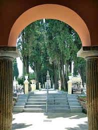 Entrada arqueada con columnas que da acceso a un jardín arbolado en la plaza