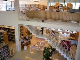 Interior de la biblioteca con escalera central, estanterías y zona de lectura en dos niveles