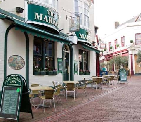 Vista de la terraza exterior de The Market Inn con mesas y sillas en calle adoquinada