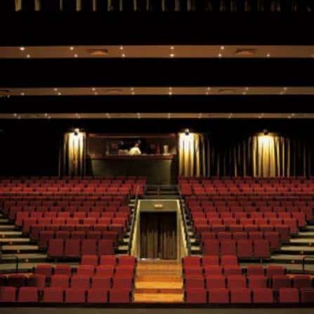 Interior del auditorio con butacas rojas y escenario iluminado
