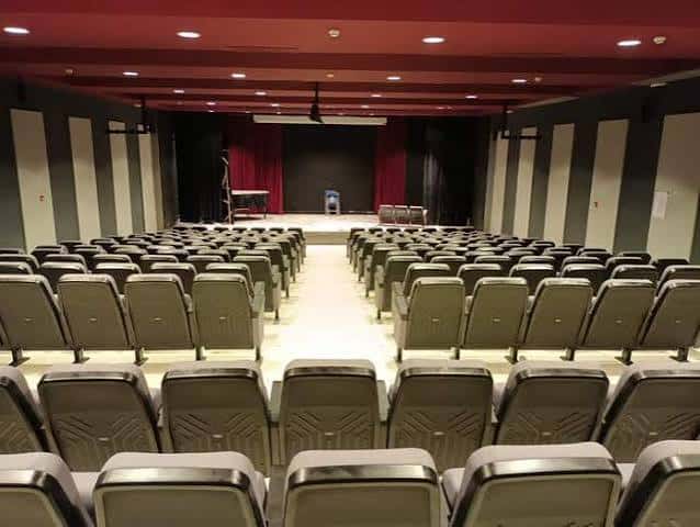 Sala de eventos con butacas grises y escenario con cortinas rojas