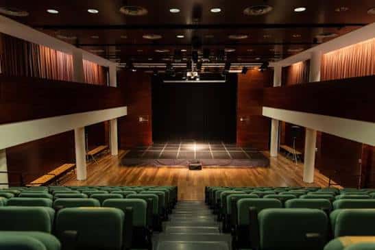 Interior del auditorio con butacas verdes y escenario iluminado