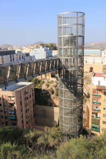 Detalle del ascensor de cristal y puente de acero con vista a la ciudad y el mar