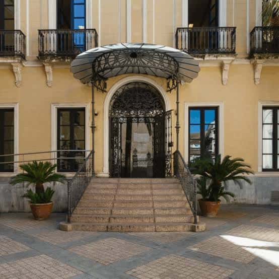 Entrada principal del edificio con escalinata y toldo metálico decorativo