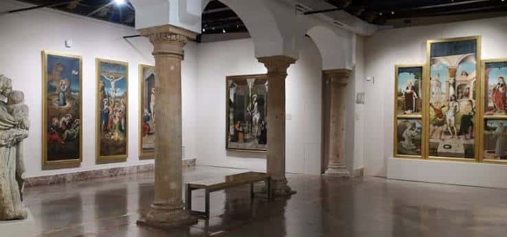 Sala de exposiciones con columnas de piedra y obras de arte religioso enmarcadas