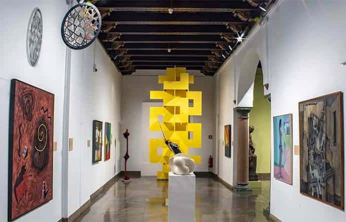 Exposición contemporánea con esculturas amarillas y obras de arte moderno en un espacio con vigas de madera