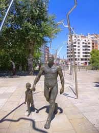 Escultura de bronce de un adulto y un niño caminando en el paseo