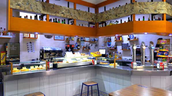 Interior del bar mostrando barra, estanterías con botellas y zona de servicio