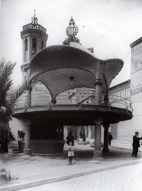 El Quiosco Modernista de la Plaça del Doctor Robert con la torre de la iglesia al fondo