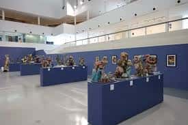 Interior del centro de arte con exposiciones en mesas azules y espacio amplio para eventos culturales