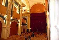 Interior del auditorio con público sentado y cortina roja en el escenario