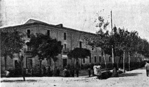 Imagen histórica en blanco y negro del Antiguo Hospital Militar en Burgos, mostrando su fachada original con árboles y personas frente al edificio