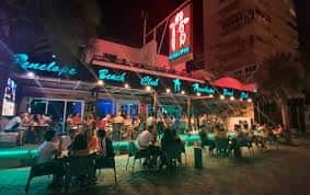 Vista nocturna de la fachada de Penélope Beach Club con luces de neón y público en terraza