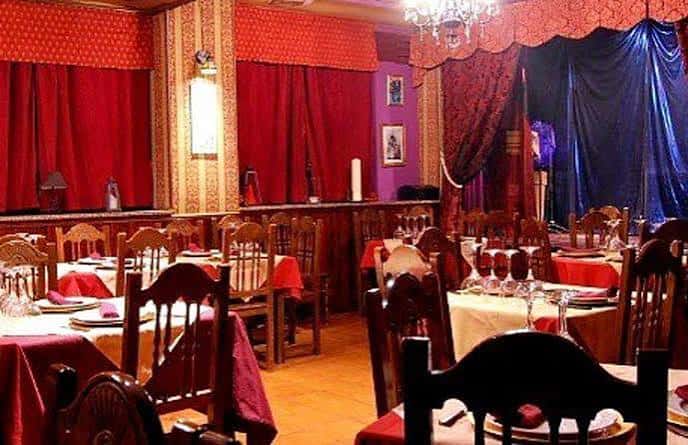 Interior del restaurante con cortinas rojas y azules, mesas con manteles y sillas de madera