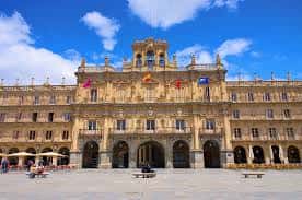 Plaza Mayor de Salamanca bajo cielo azul con banderas y bancos en primer plano