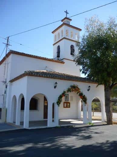 Vista frontal de la Ermita de Sanz con su fachada blanca y campanario bajo el cielo azul