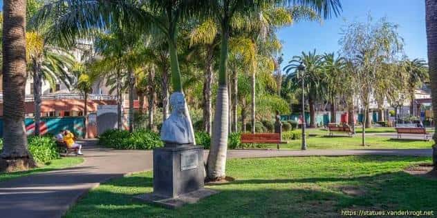 Estatua en el parque rodeada de palmeras y bancos de madera