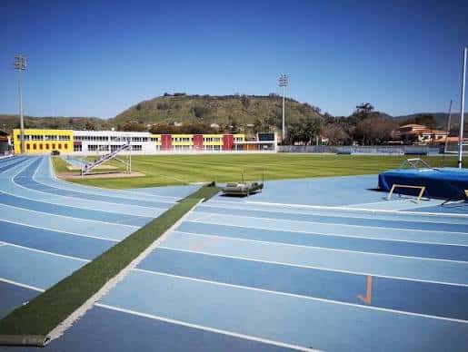 Vista general del estadio con pista de atletismo azul y edificio de gradas