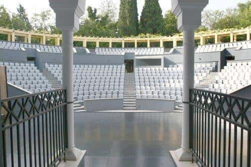 Interior del auditorio al aire libre con gradas de asientos blancos y escenario frente a un fondo de árboles