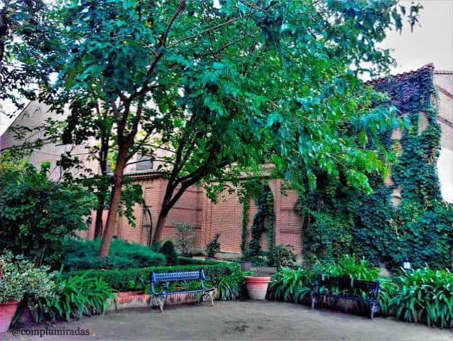Rincón del jardín con banco, vegetación y pared de ladrillo cubierta de hiedra