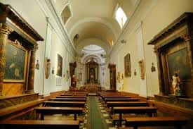 Nave central de la capilla con bancos de madera y obras de arte en las paredes