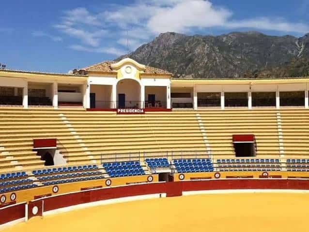 Vista interior de la plaza de toros con gradas amarillas y montañas al fondo