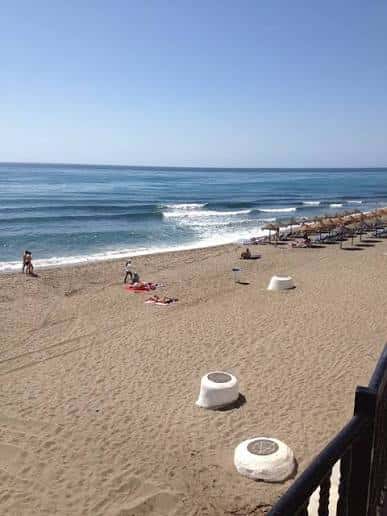 Vista de la playa con olas rompiendo y personas disfrutando del sol