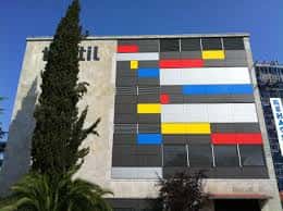 Detalle arquitectónico de la fachada del museo con paneles de colores y árbol alto al lado
