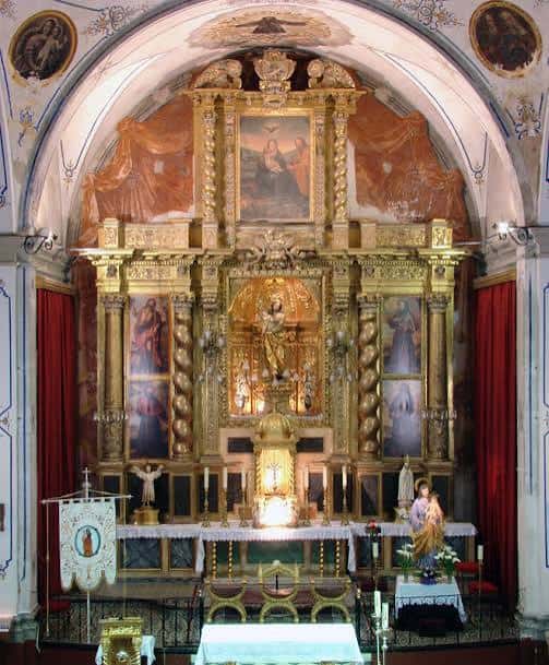 Altar principal dorado con pinturas religiosas y cortinas rojas
