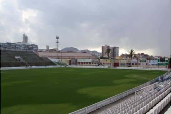 Vista panorámica del campo de fútbol con gradas y ciudad de fondo