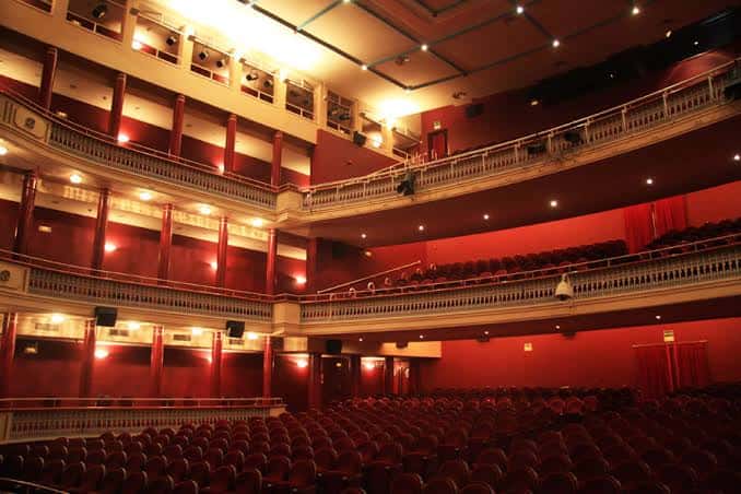 Vista lateral del interior del teatro con iluminación cálida y múltiples niveles de palcos