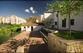 Paseo ajardinado con acceso al edificio cultural y vista de la montaña al fondo