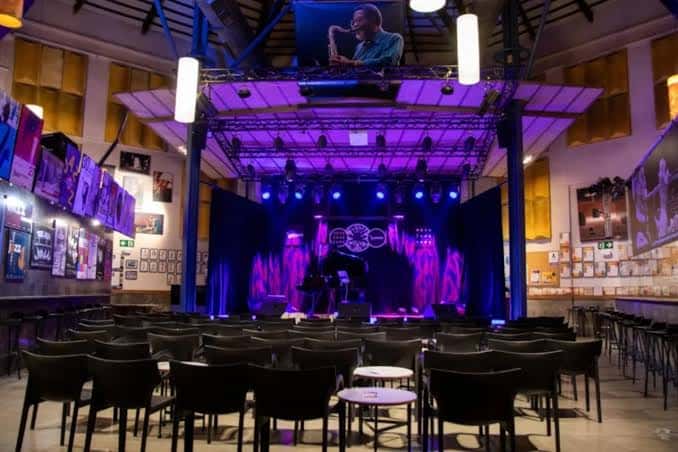 Vista interior del auditorio Nova Jazz Cava con escenario iluminado en tonos morados y butacas vacías listas para el evento
