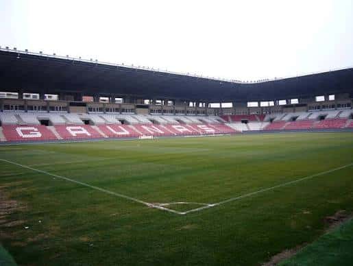 Vista panorámica del interior del estadio con gradas rojas y blancas y campo de césped