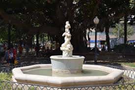 Fuente ornamental en el centro del parque rodeada de árboles y bancos