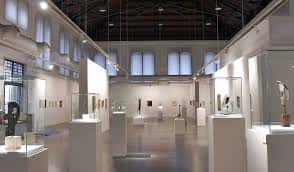 Interior de la sala de exposiciones con vitrinas, esculturas y iluminación natural desde ventanas altas