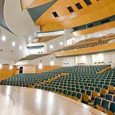 Interior del auditorio con gradas curvas, butacas verdes y escenario de madera