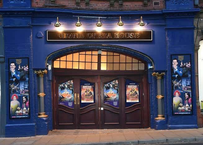 Entrada nocturna del Grand Opera House con fachada azul, luces doradas y carteles de espectáculos