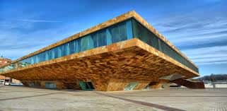 Vista exterior del Teatre de la Llotja con su distintiva fachada de madera y cristal bajo un cielo azul